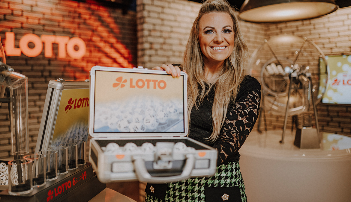 Lottomoderatorin hält Koffer mit Probekugeln Lotto 6aus49