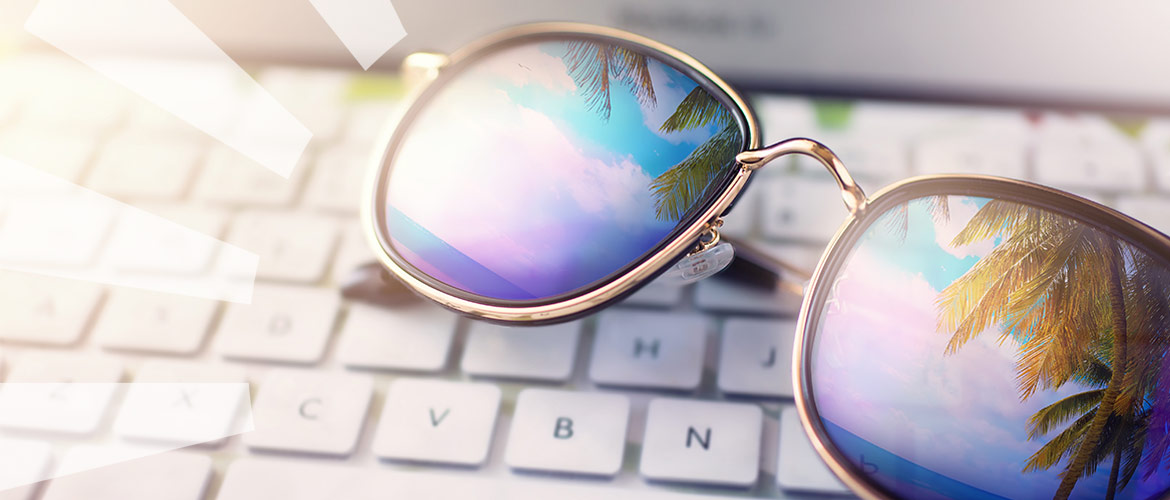 Sonnenbrille auf Computertastatur in der sich Palmen und das Meer spiegeln